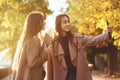 Side profile of young smiling brunette twin girls taking a selfie with black phone, while one of them is holding books Royalty Free Stock Photo