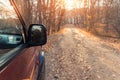 Side rear mirror view of SUV car drive on beautiful dirt gravel forest unpaved road in autumn foliage and bright warm Royalty Free Stock Photo