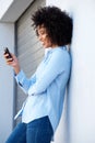 Side of relaxed young african woman using a mobile phone leaning to a wall outdoors Royalty Free Stock Photo
