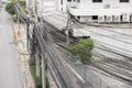 On the side of a road in Thailand there is an electric pole with a mess of wires and buildings and trees behind it