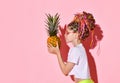 Side shot of cute girl with colorful braids in stylish red glasses looking on big pineapple in hands and going to kiss it