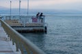 Side shot of a male and female standing on the boardwalk with a metal fence on Tiberias harbor