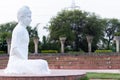 Side shot of a white colored Buddha statue in meditative pose with green trees and concrete strunctures behind Royalty Free Stock Photo