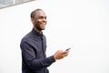 Side of smiling African American man holding mobile phone by white wall Royalty Free Stock Photo