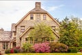 Side of upscale three story rock home with pink azaleas and dogwood tree in full bloom in Springtime