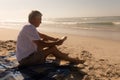 Senior man reading a book while relaxing on picnic blanket at beach Royalty Free Stock Photo