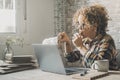 Side view of adult woman eating cookies sitting at the desk table in front of an open laptop and things to do. Busy entrepreneur Royalty Free Stock Photo