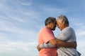 Side view of affectionate multiracial senior couple embracing while touching foreheads against sky