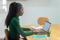 Side view at african-american female office employee using headset and laptop sitting on the workplace Royalty Free Stock Photo