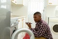 Man talking on mobile phone while putting clothes in washing machine in kitchen Royalty Free Stock Photo