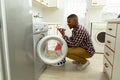Man talking on mobile phone while putting clothes in washing machine in kitchen Royalty Free Stock Photo