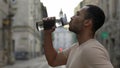 Side view african american runner drinking water from the sport bottle after the scamper. Man feels thirsty after