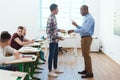 Side view of african american teacher pointing at wristwatch to latecomer schoolboy