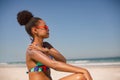 Woman in bikini applying sunscreen lotion on shoulder at beach in the sunshine