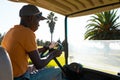 Side view of african american young man wearing cap driving golf cart against sky at golf course Royalty Free Stock Photo