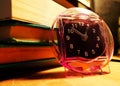 Side view of an alarm clock standing next to a pile of books on a wooden surface Royalty Free Stock Photo