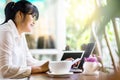 Side view of Asian businesswoman sitting at long table in coffee shop and using laptop computer and chatting on cell phone. Freela Royalty Free Stock Photo