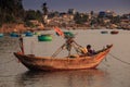 Side View Asian Fisherman Sits in Boat by Bank against Village