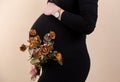 Side view of an attractive pregnant woman caressing her belly and holding a bouquet of dry roses in black dress while standing Royalty Free Stock Photo