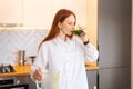 Side view of attractive redhead young woman drinking healthy vegetable detox smoothie juice from blender standing in Royalty Free Stock Photo