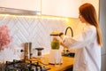 Side view of attractive redhead young woman making healthy vegetable detox smoothie juice in blender standing in kitchen Royalty Free Stock Photo