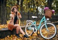 Happy woman sitting near bicycle in urban autumn park.