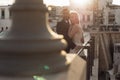 Side view of attractive wedding couple standing at steel railing of bridge at sunset. Young bride embracing with groom. Royalty Free Stock Photo