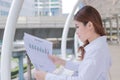 Side view of attractive young Asian business woman analyzing paperwork or charts in her hands at outside office. Royalty Free Stock Photo