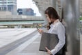 Side view of attractive young Asian business woman holding document folder and looking mobile smart phone in her hands at outside Royalty Free Stock Photo