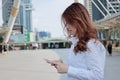 Side view of attractive young Asian business woman looking mobile smart phone in her hands at urban building city background. Royalty Free Stock Photo