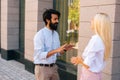 Side view of attractive young blonde business woman and Indian bearded business man talking outdoors by office building. Royalty Free Stock Photo