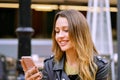 Side view of attractive young lady smiling and browsing modern smartphone