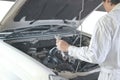 Side view of automotive mechanic in white uniform with wrench diagnosing engine under hood of car at the repair garage. Royalty Free Stock Photo