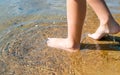 Side view of bare feet of caucasian child in water on sand outdoors on summer sunny day. Royalty Free Stock Photo