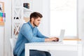 Side view of a bearded casual businessman sitting with laptop