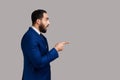 Side view of bearded man looks at camera with surprised amazed expression, points away at copy space Royalty Free Stock Photo