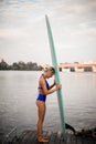 Side view of beautiful blonde woman who stands on wooden pier with surfboard in her hands Royalty Free Stock Photo