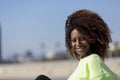 Side view of a beautiful curly afro woman sitting on breakwater rocks laughing while looking camera outdoors Royalty Free Stock Photo