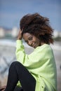 Side view of a beautiful curly afro woman sitting on breakwater rocks laughing while looking camera outdoors Royalty Free Stock Photo