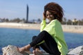 Side view of a beautiful curly afro woman sitting on breakwater rocks laughing while looking camera outdoors Royalty Free Stock Photo