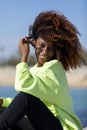 Side view of a beautiful curly afro woman sitting on breakwater rocks laughing while looking camera outdoors Royalty Free Stock Photo