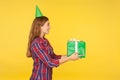 Side view of beautiful positive good natured girl with funny party cone on head giving present and saying congratulations