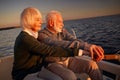 Side view of beautiful senior couple sailing at sunset, elderly man and woman sitting on the side of boat or yacht deck Royalty Free Stock Photo