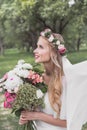 side view of beautiful smiling young bride in veil holding wedding bouquet Royalty Free Stock Photo