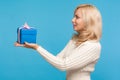 Side view beautiful woman with curly blond hair holding blue gift box in hands, making present, donation, charity concept