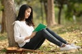 Side view of beautiful young Asian woman reading book at the park with ukulele at her side, concept leisure hobby time, reading is Royalty Free Stock Photo