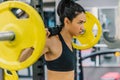 Side view of beautiful young woman doing workout in the gym, pushing yellow barbell on shoulders. Female hard workout for cross