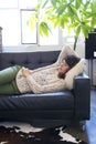 Side view of beautiful young woman lying on leather couch relaxing while looking away at home Royalty Free Stock Photo