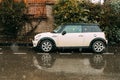 Side View Of beige white Color Mini Cooper S Car Parked On Street near old house.