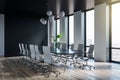 Side view on big black meeting table among light office chairs on wooden floor in stylish sunlit conference room with city view